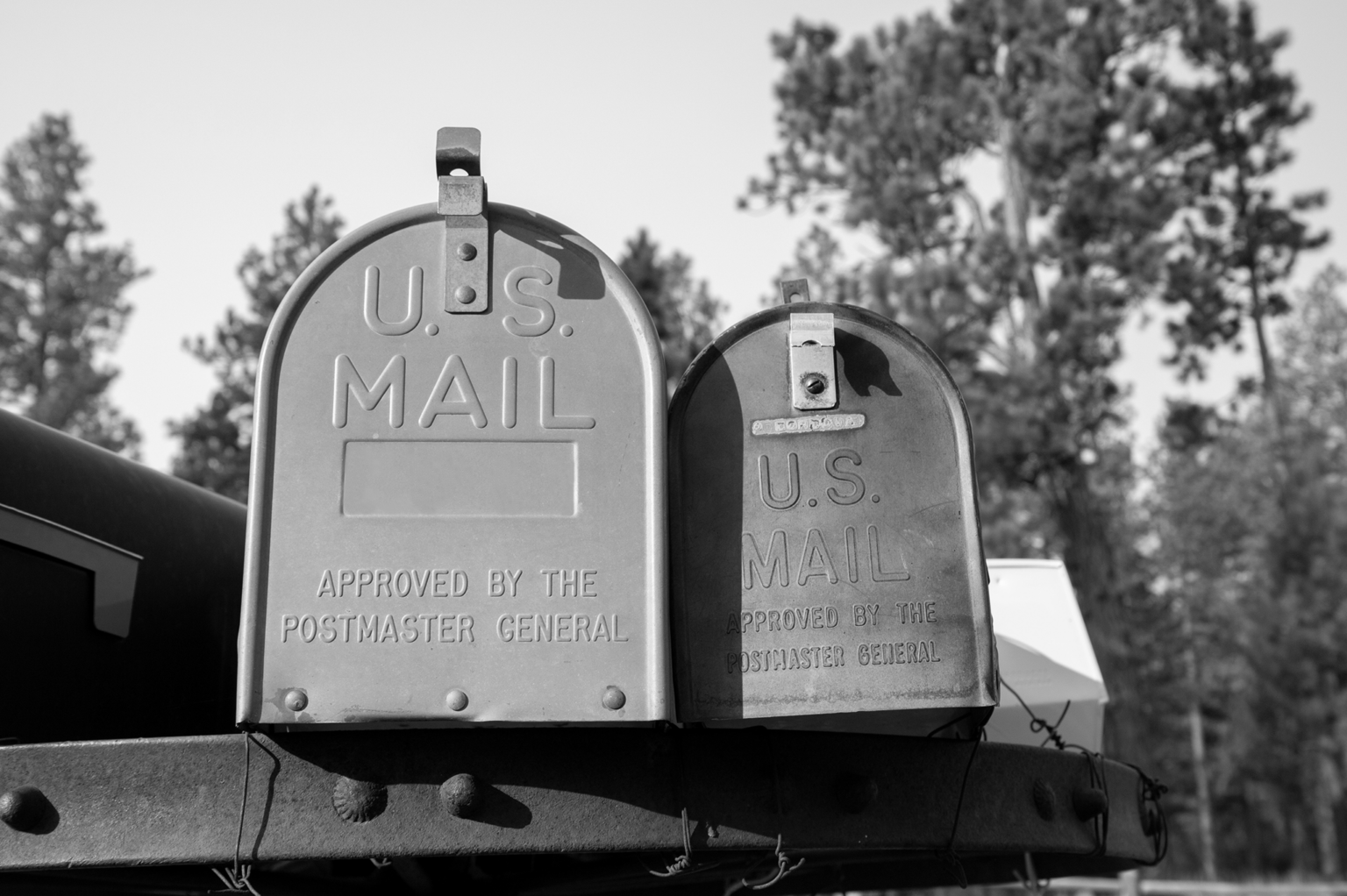 Black and white photo of 2 US Mail boxes on the side of the road.