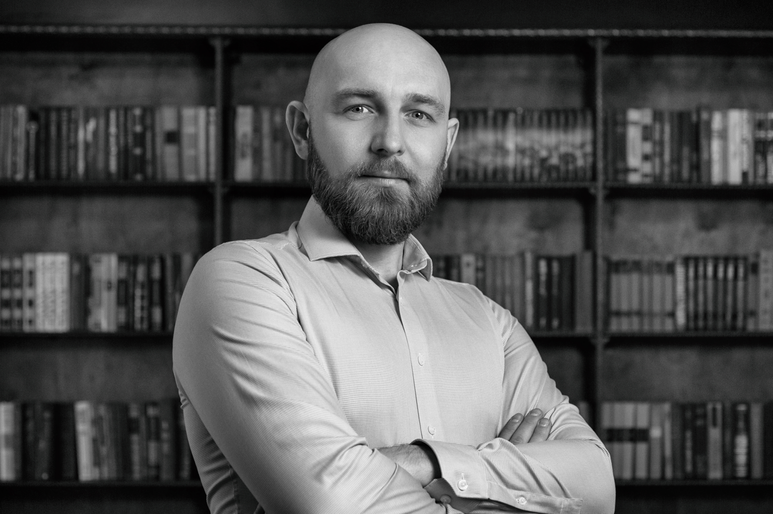 Black and white photo of a bald man with a full beard with his arms crossed.