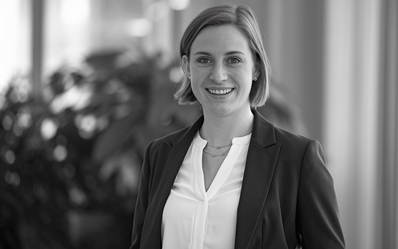 Black and white photo of a young white woman smiling at the camera. She is wearing a white blouse and dark suite jacket.