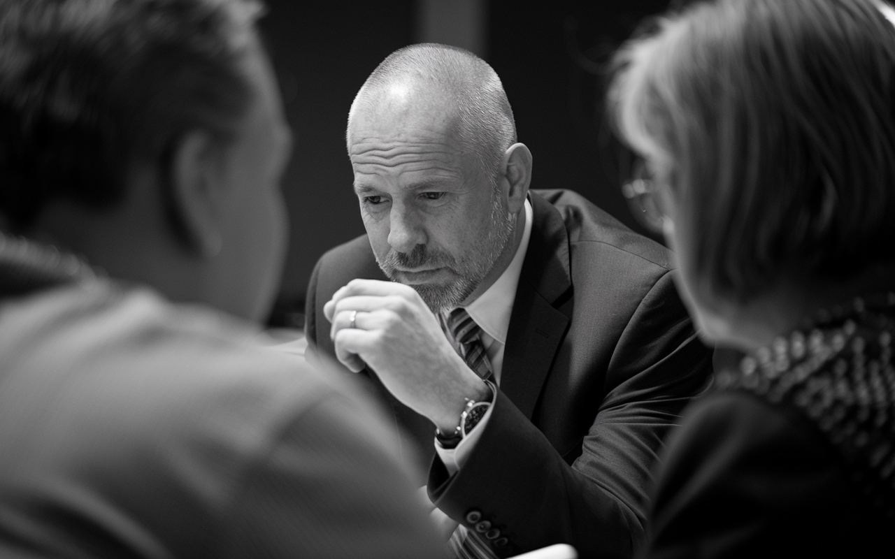 Black and white photo of a bald white man with a beard in a suit looking down.