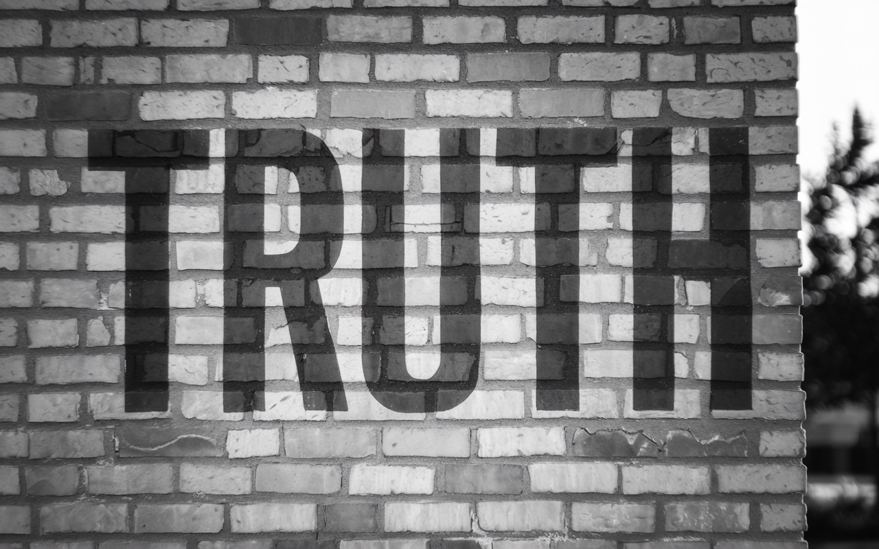 Black and white photo of the word truth painted on a brick wall